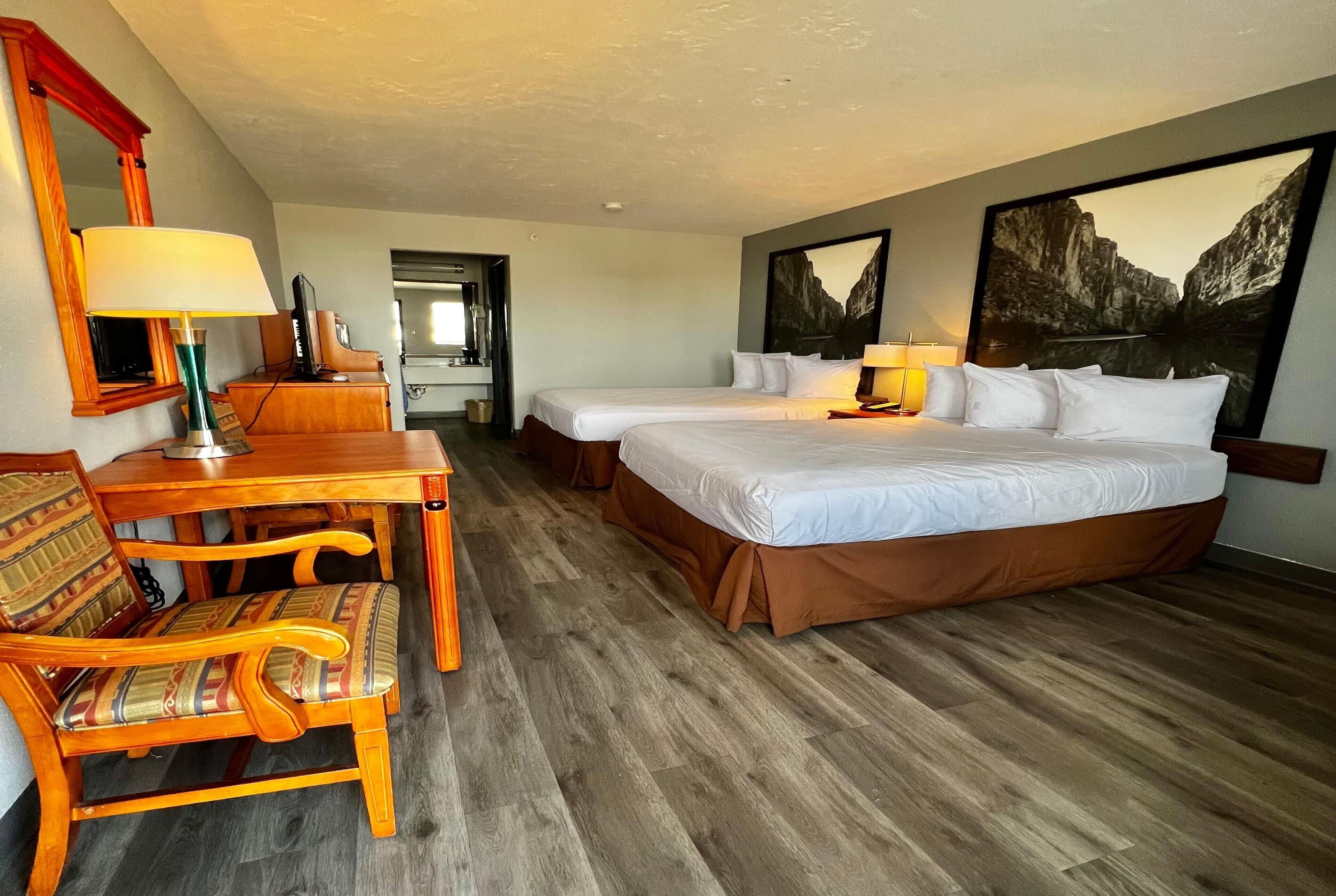 A hotel room with two beds, a wooden desk, a chair, a mirror, and a painting on the wall.