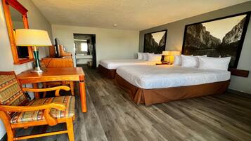 A hotel room with two beds, a wooden desk, a chair, a mirror, and a painting on the wall.
