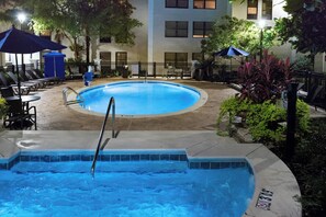 A swimming pool with a hot tub, surrounded by outdoor seating and a building in the background.