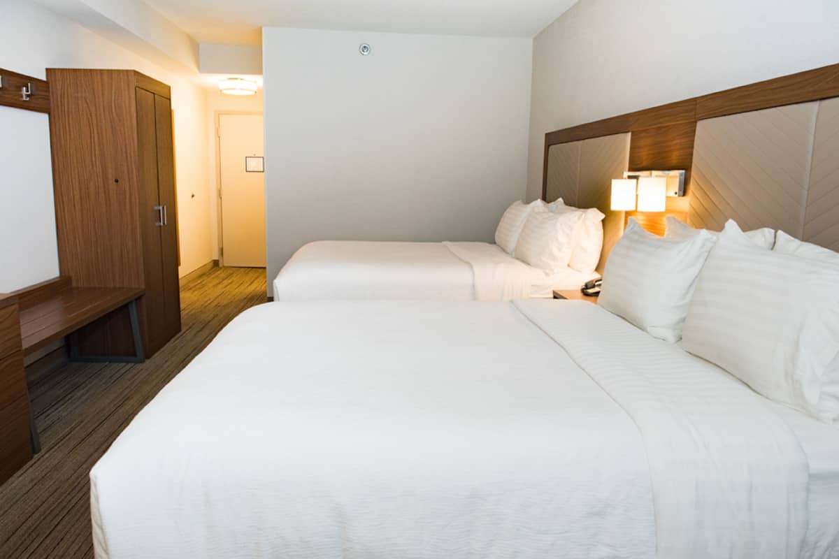A hotel room with two beds, a wooden wardrobe, and a nightstand with a lamp.