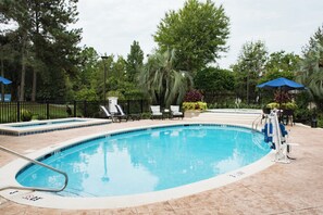 Una piscina con borde de azulejos, rodeada por una valla negra y equipada con una escalera.