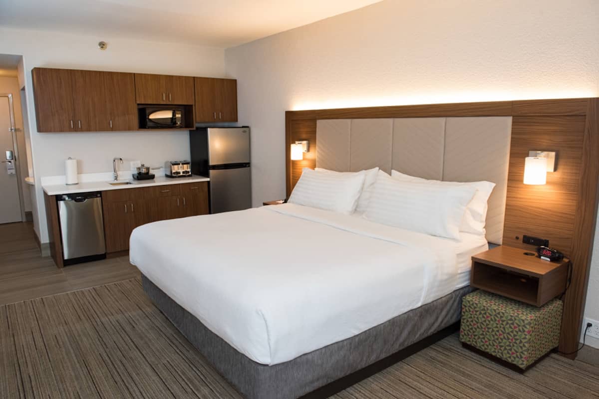 A hotel room with a large bed, a bedside table, a nightstand, a microwave, a refrigerator, and a small kitchenette.