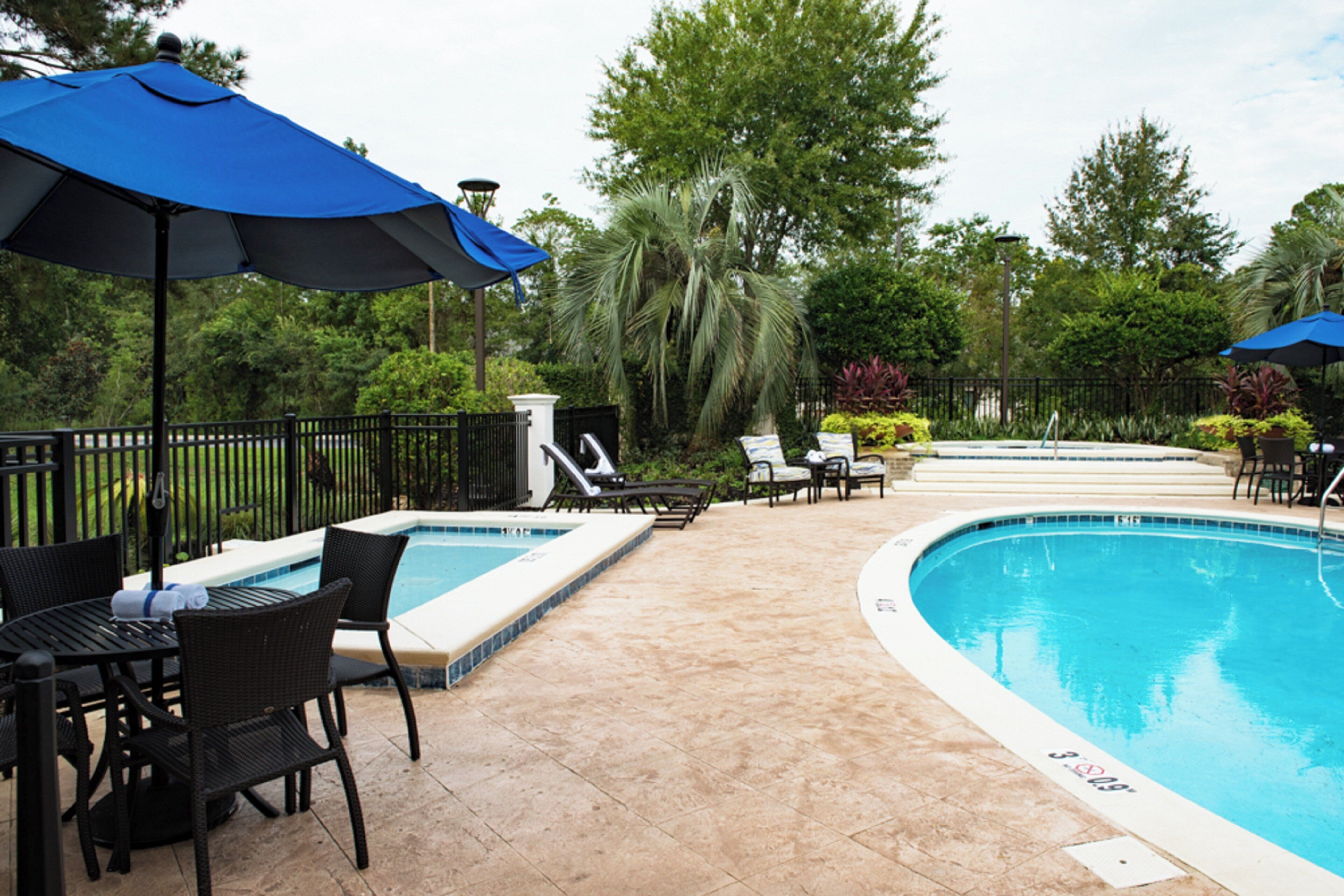 A pool area with lounge chairs, umbrellas, and a tiled deck.