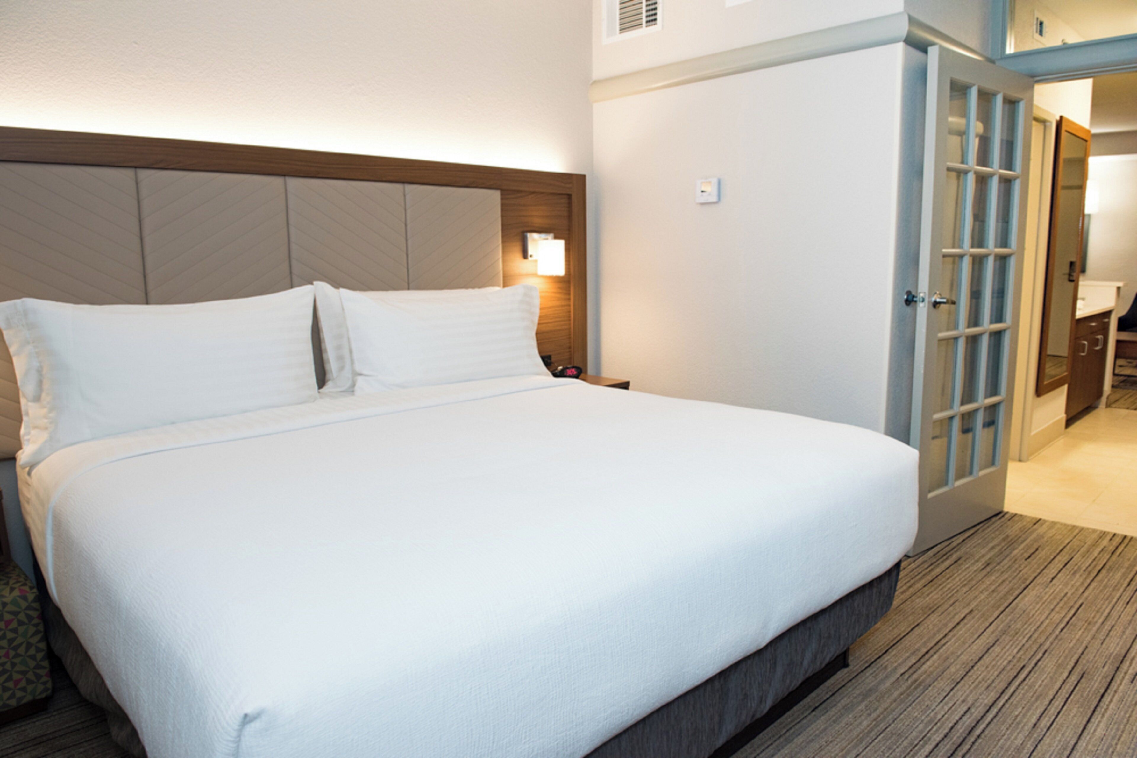 Habitació d'hotel amb un llit gran, un panell de capçal de fusta, una taula de nit i una porta que dona a un bany.
