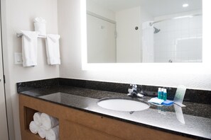 A bathroom with a sink, mirror, and towels on a shelf.
