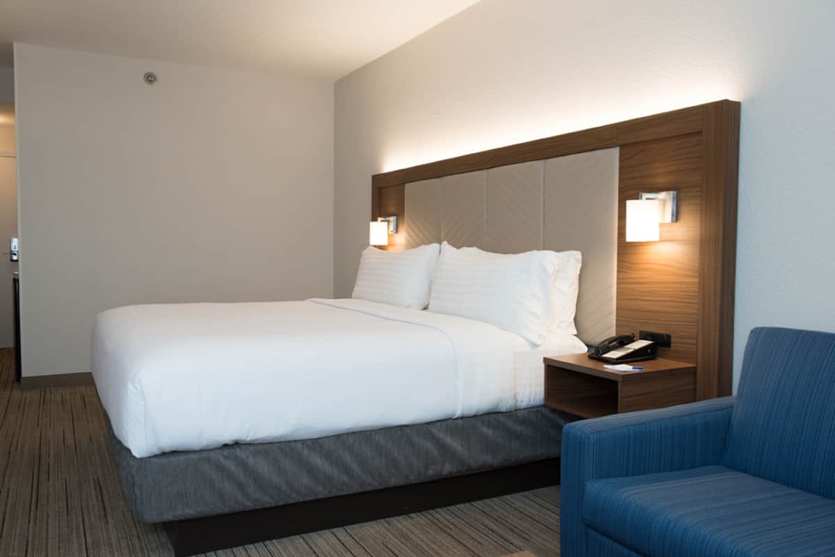 A hotel room with a large bed, a bedside table with a phone, and a blue chair.