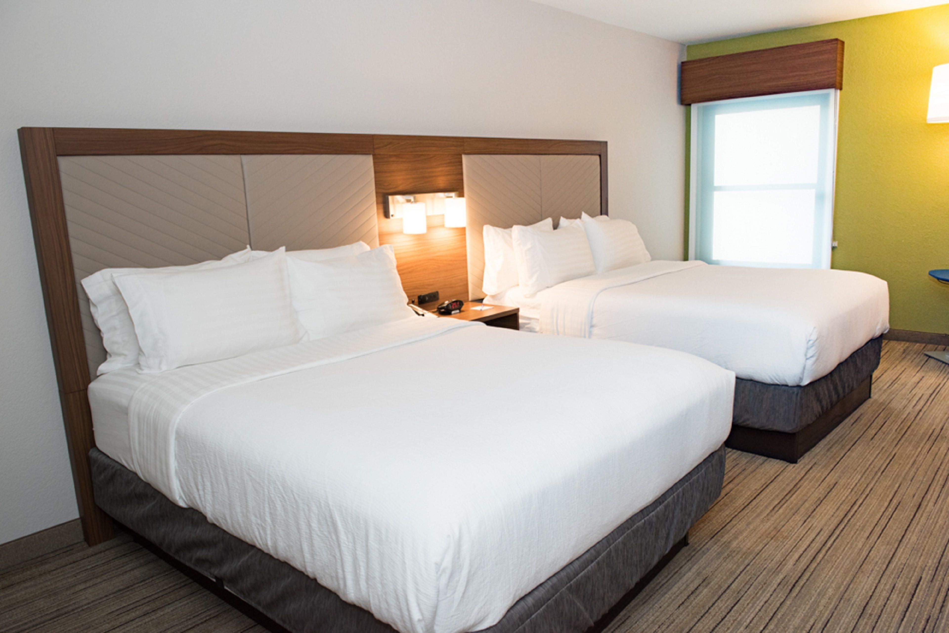 A hotel room with two beds, a nightstand with a lamp, and a window with a view of the outside.