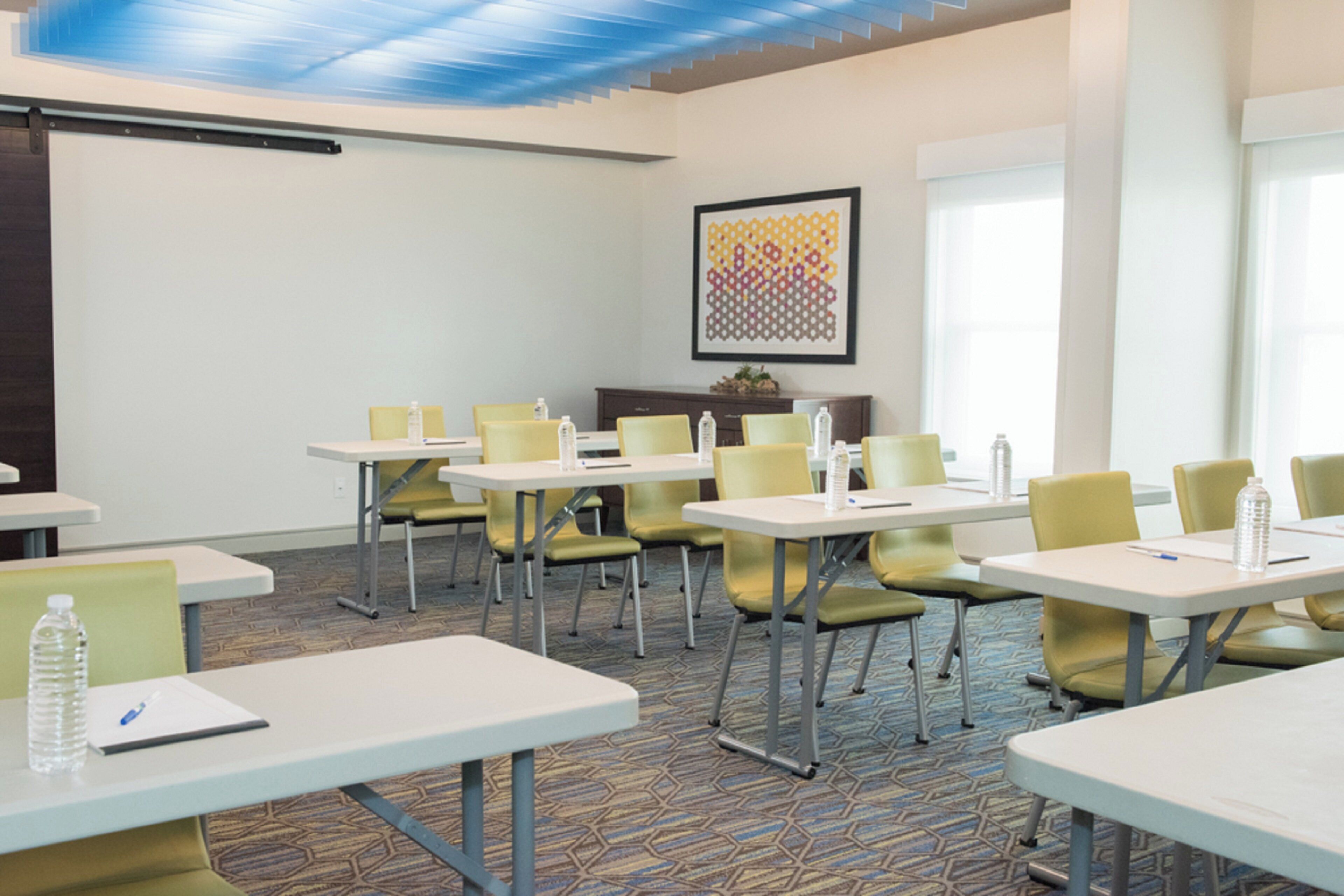 A conference room with tables and chairs, a water dispenser, and a framed artwork on the wall.