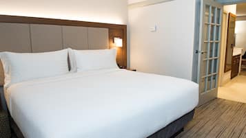 Una habitación de hotel con una cama grande, un cabecero de madera, una mesita de noche y una puerta que da a un baño.