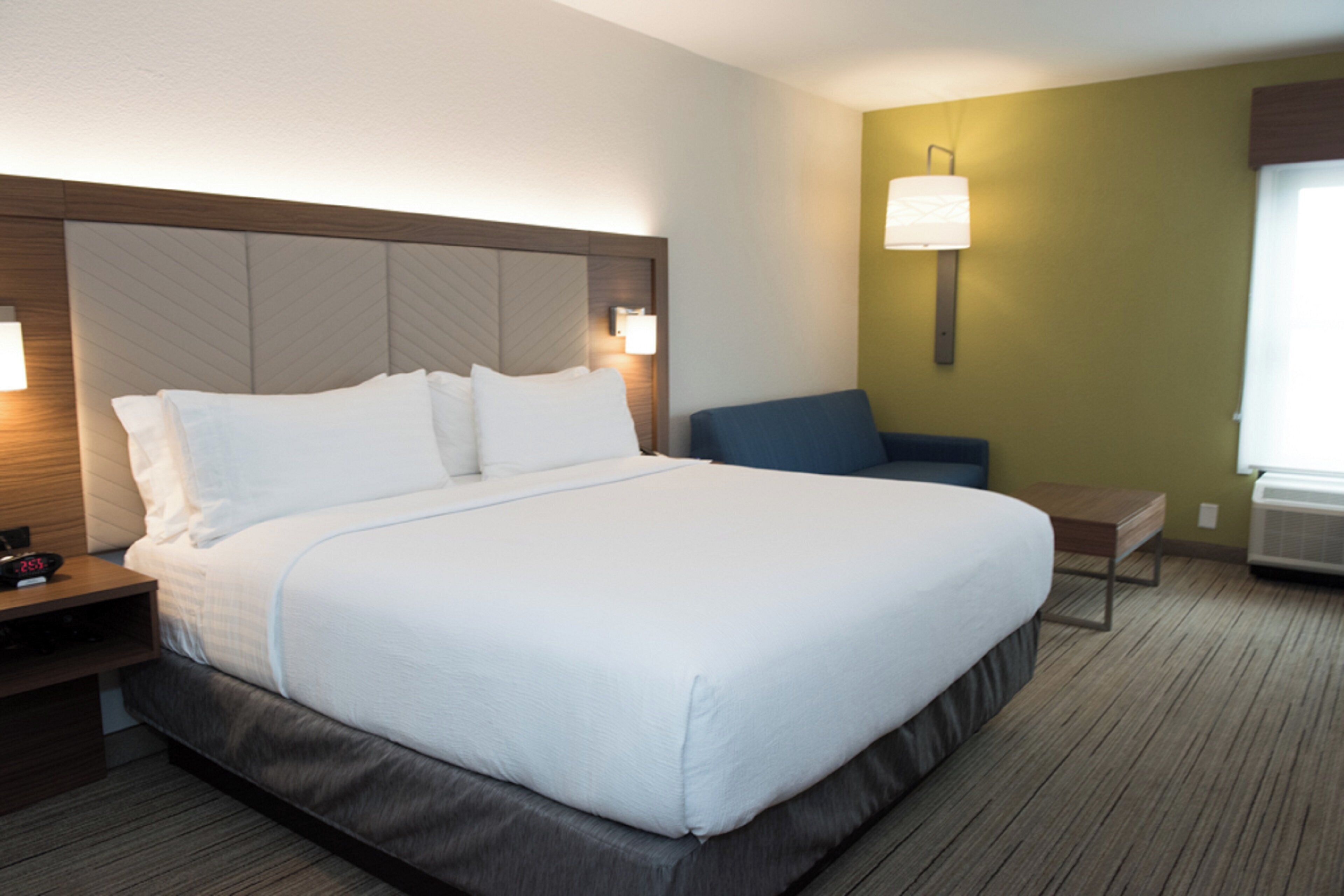 A hotel room with a large bed, bedside tables, a chair, and a lamp.