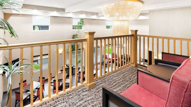 A hotel lobby with a high ceiling, a chandelier, a staircase, and a dining area with red chairs and tables. - Comfort Suites Portland Airport (Portland)