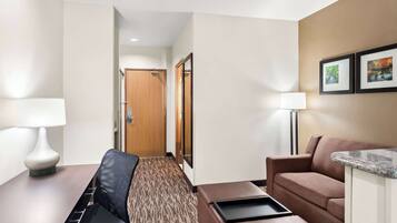 A hotel room with a desk, chair, couch, and a small kitchenette.