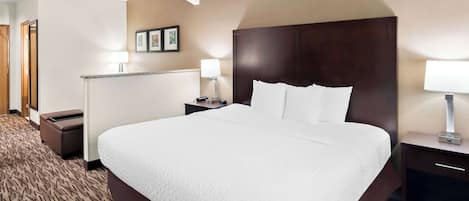 A hotel room with a large bed, a nightstand with a lamp, a trash bin, and a wall-mounted picture.