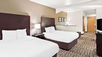 A hotel room with two beds, a desk, a TV, and a bathroom door.