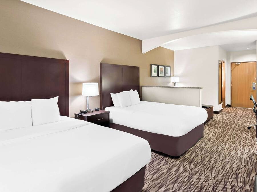 A hotel room with two beds, a desk, a TV, and a bathroom door.