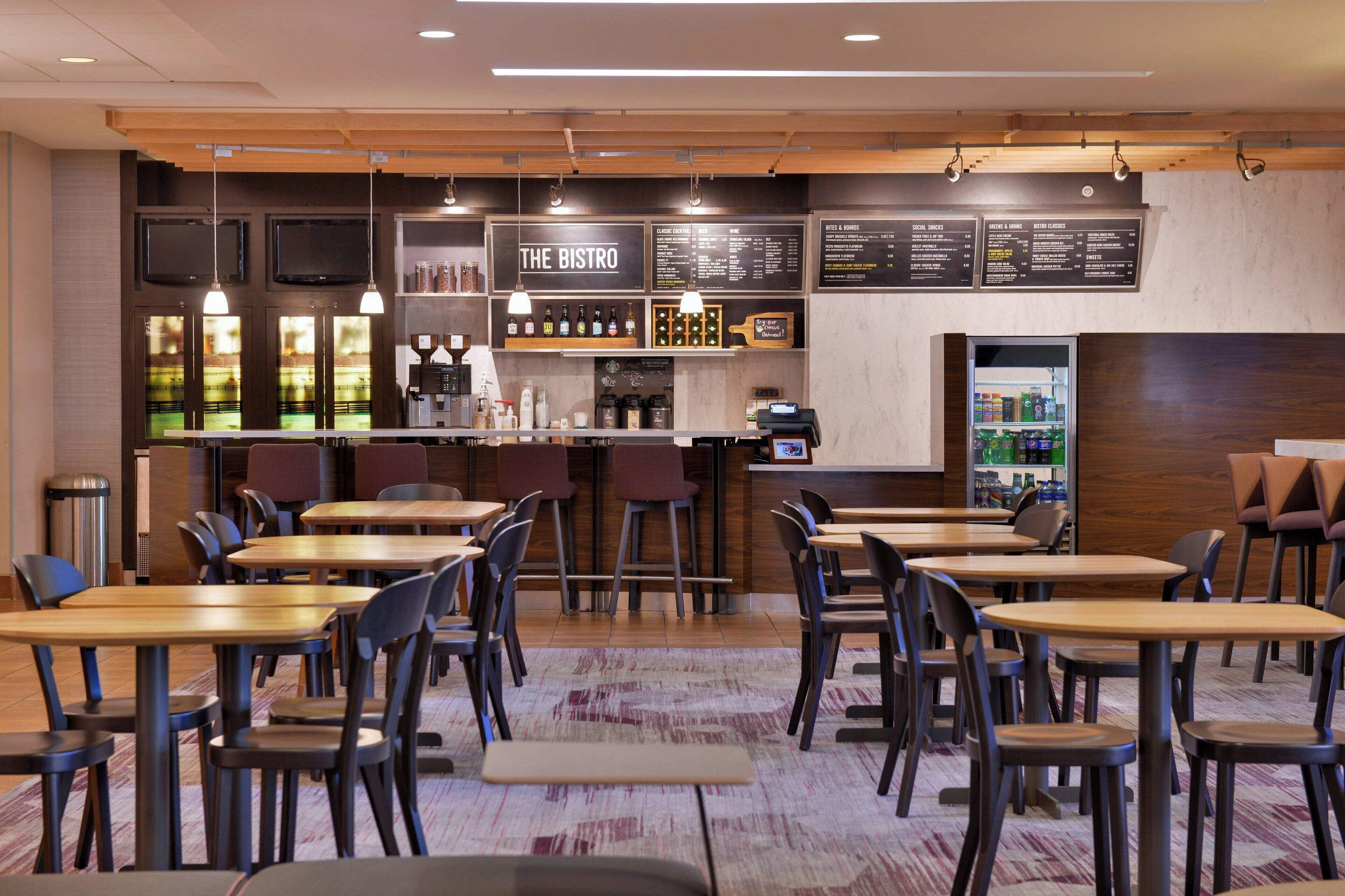 Un restaurante con mesas y sillas de madera, una zona de bar y pizarras con la carta.