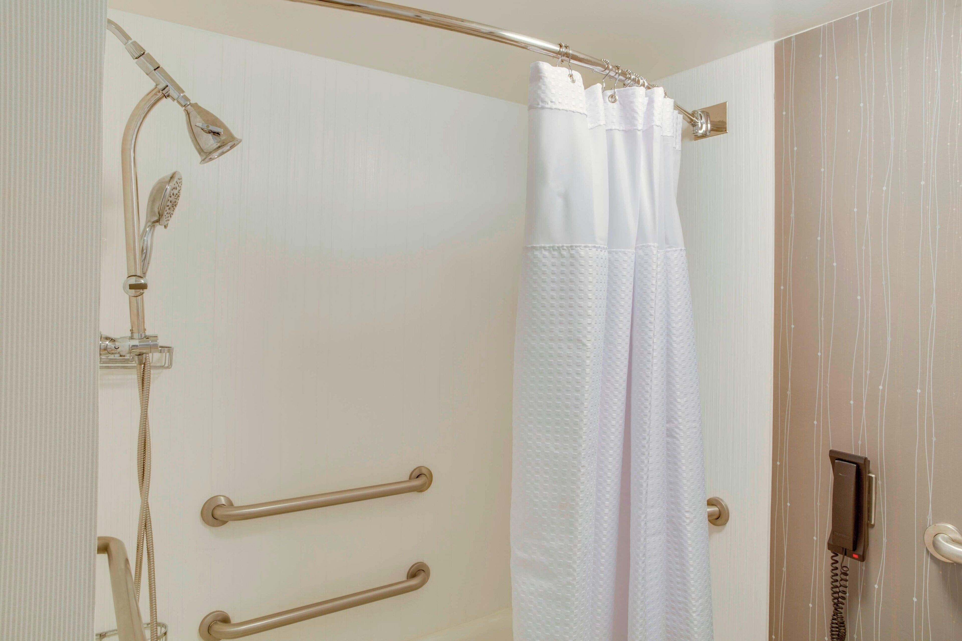 A shower area with a handheld showerhead, a white shower curtain, and two grab bars.