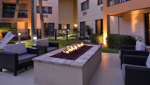 Un espacio de estar al aire libre con mobiliario de mimbre y una chimenea central.