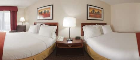 A hotel room with two beds, a desk, a lamp, and two paintings on the wall.