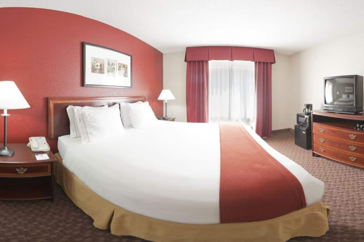 Habitación de hotel con una cama grande, dos mesitas de noche con lámparas, un televisor en una cómoda y una ventana con cortinas.