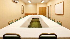 Un salón de conferencias con una larga mesa, sillas, un televisor y un cuadro enmarcado en la pared.