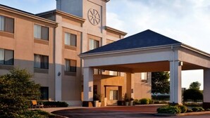 Un hotel moderno con una torre de reloj central, un acceso cubierto y una entrada arbolada.