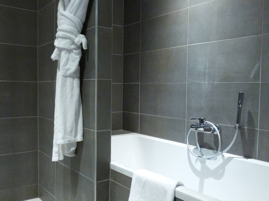 Un baño moderno con baldosas oscuras, una bañera blanca y una bata blanca colgada en la pared.