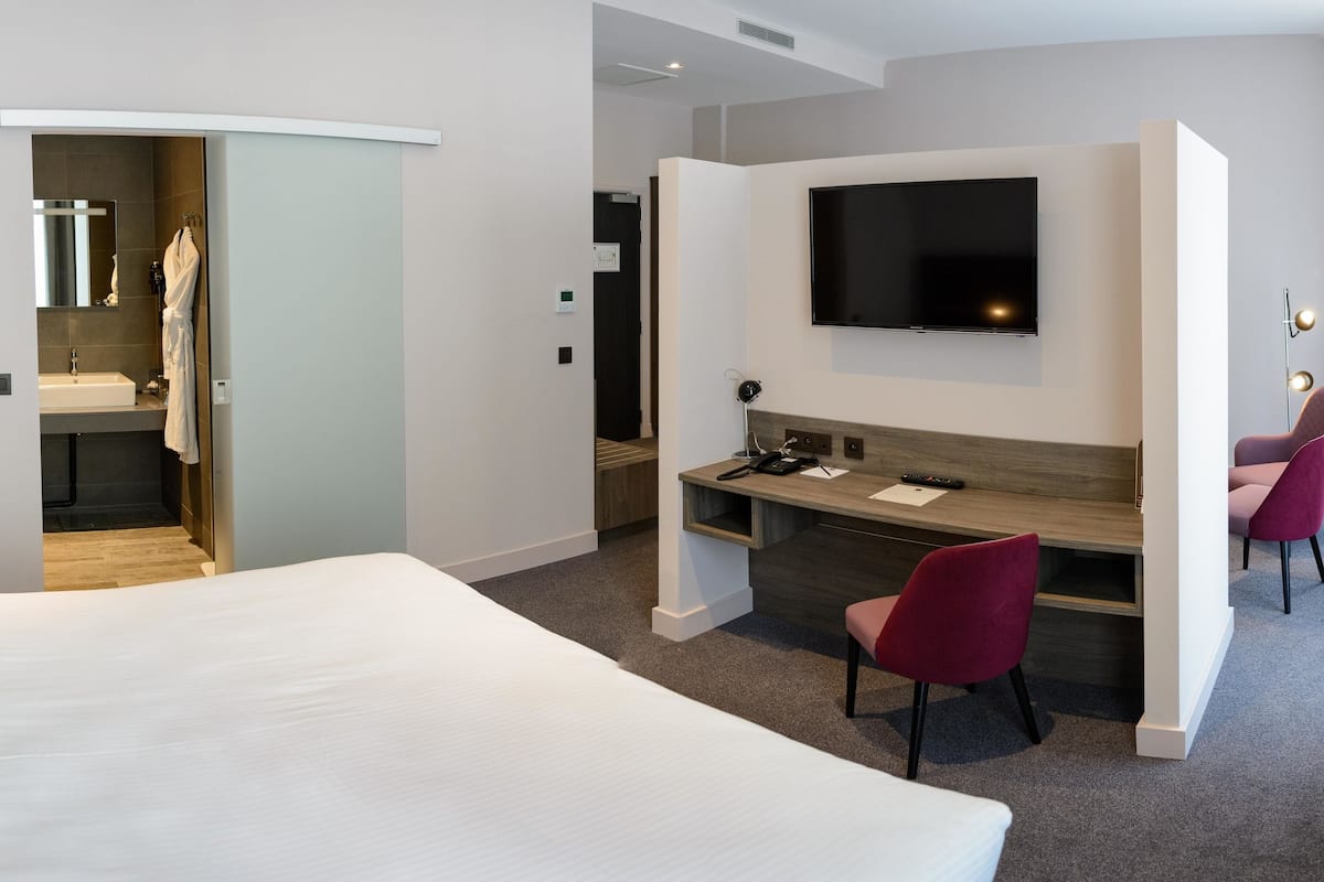 A modern hotel room with a large bed, a desk, a TV, and a chair.