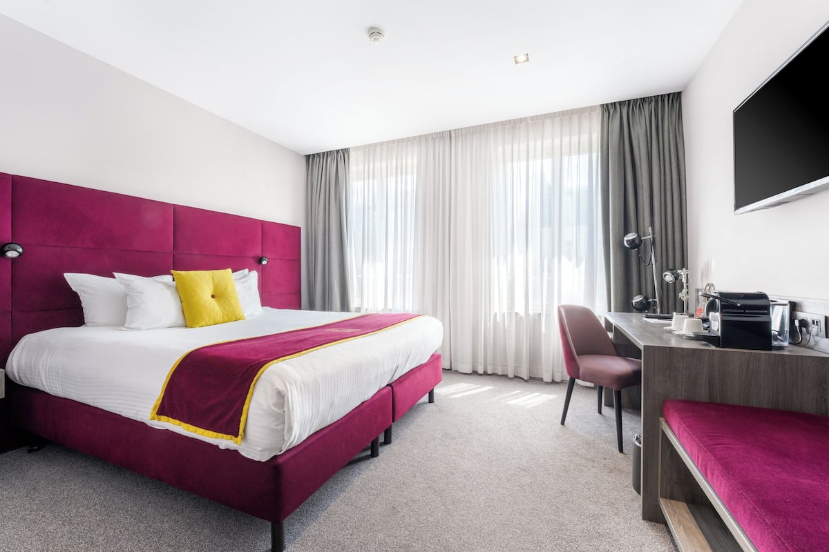 A hotel room with a large bed, a desk, a chair, and a TV.