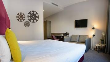 A hotel room with a large bed, a sofa, a desk with a chair, a TV, and decorative wall art.