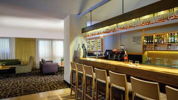 A bar area with a long counter, bar stools, and shelves with bottles and glasses.