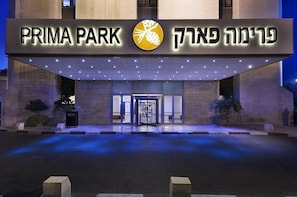 Exterior de un hotel llamado "PRIMA PARK" con una entrada destacada y señalización iluminada.