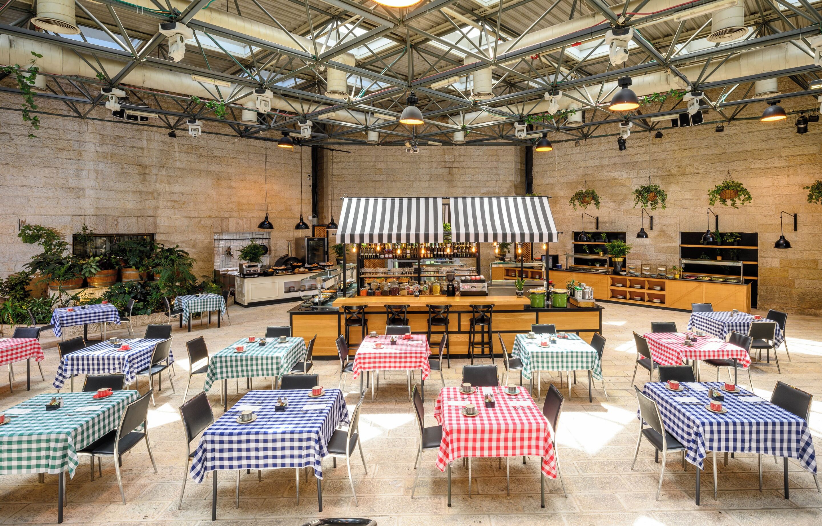 Un amplio comedor interior con varias mesas y sillas, una zona de bar central y diversas plantas y adornos.