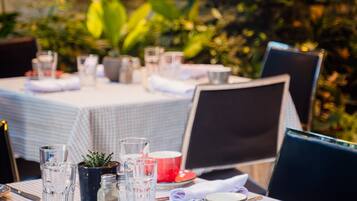 A table set for dining outdoors with a checkered tablecloth, glasses, cutlery, and a red cup.