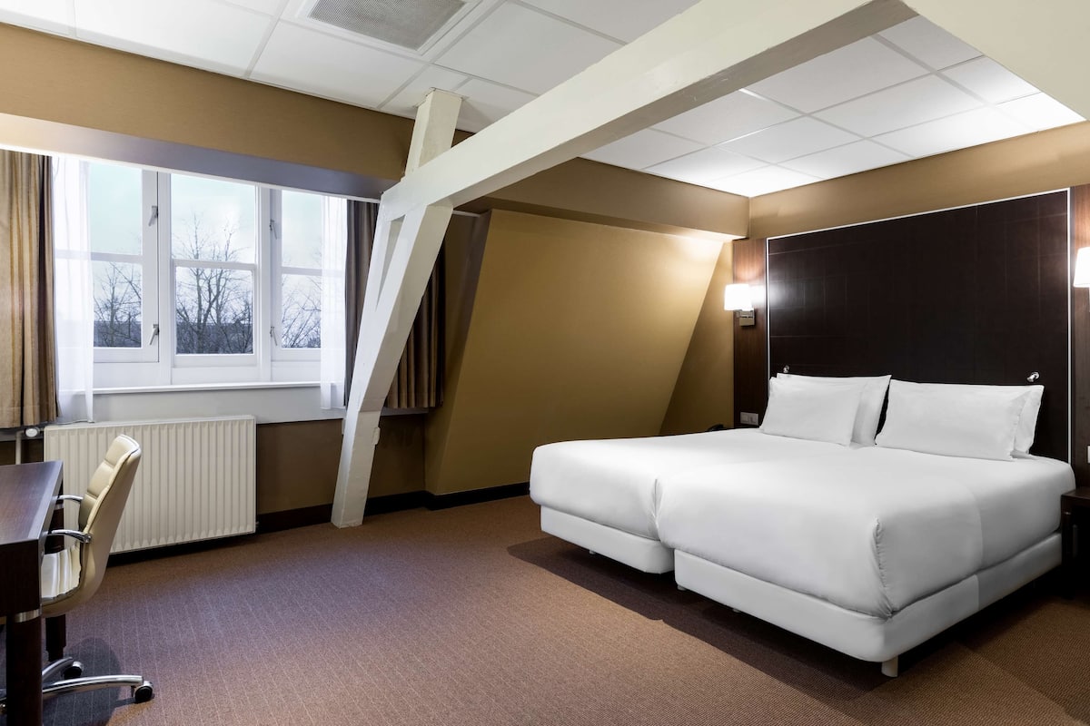 Una habitación de hotel con una cama grande, un escritorio y una ventana con cortinas.