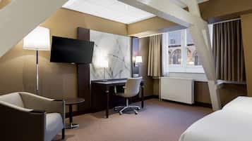 A hotel room with a bed, a desk, a chair, a TV, and a window with curtains.