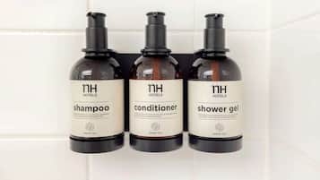 Three bottles of hotel amenities: shampoo, conditioner, and shower gel, labeled with 'nh hotels' and 'green tea'.
