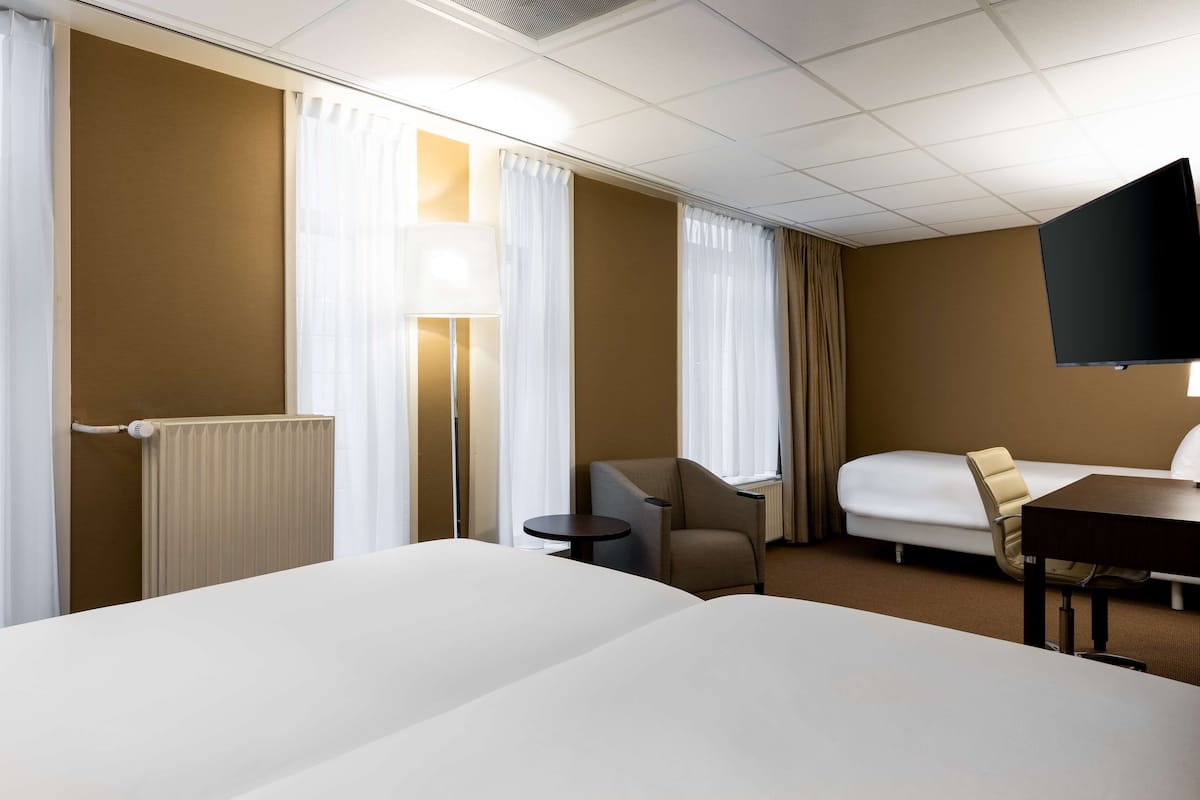 Habitación de hotel con dos camas, un escritorio, una silla, un televisor y una ventana con cortinas.