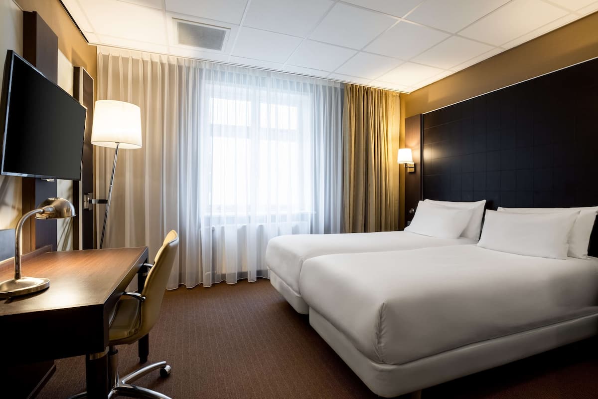 Habitación de hotel con una cama grande, un escritorio con lámpara, un televisor y una ventana con cortinas.