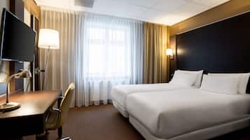 Habitación de hotel con una cama grande, un escritorio con lámpara, un televisor y una ventana con cortinas.