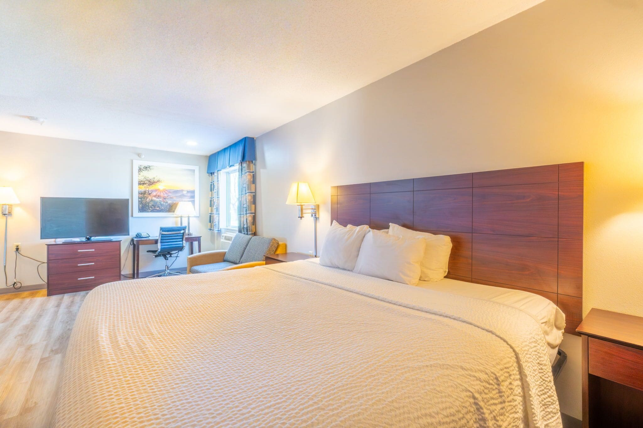 A hotel room with a large bed, a desk with a chair, a television, and two bedside lamps.