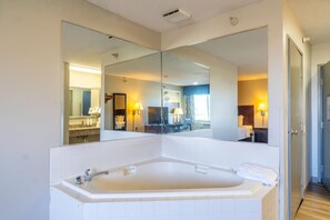 A modern bathroom with a large bathtub, a mirror, and a view into the adjacent room.