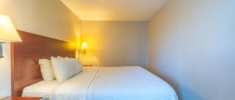 Habitación de hotel con cama, cabecero de madera, mesita de noche y lámpara de pared.
