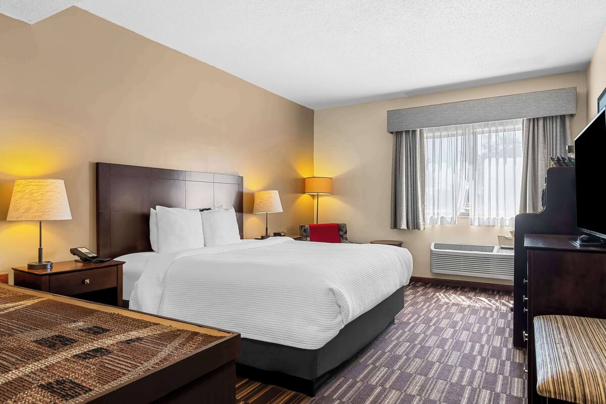 A hotel room with a large bed, bedside lamps, a desk with a lamp, a TV, and a window with curtains.