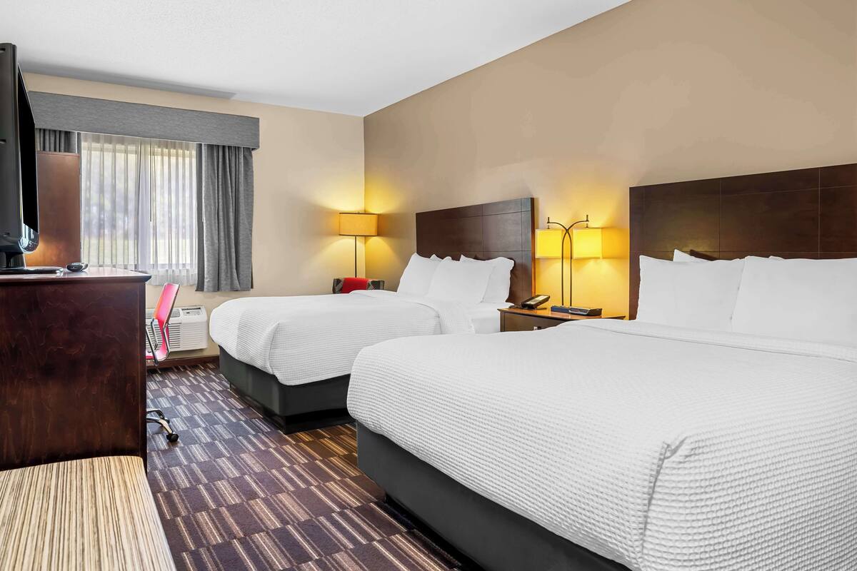 A hotel room with two beds, a desk, a TV, and two bedside lamps.