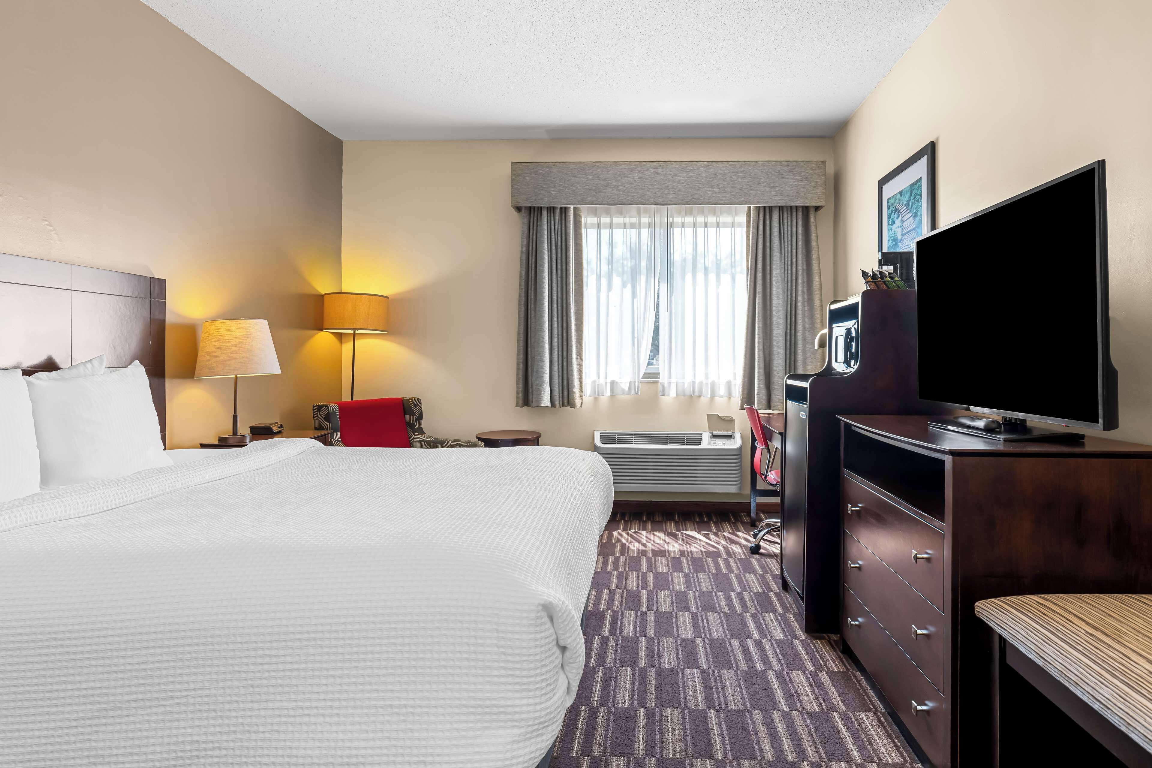 A hotel room with a large bed, a desk with a lamp, a television, and a window with curtains.