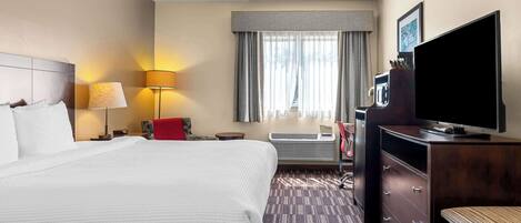 A hotel room with a large bed, a desk with a lamp, a television, and a window with curtains.