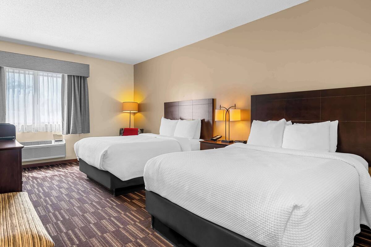 A hotel room with two beds, a desk, a chair, and a window with curtains.