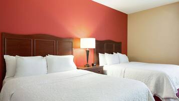A hotel room with two beds, a nightstand, and a lamp.