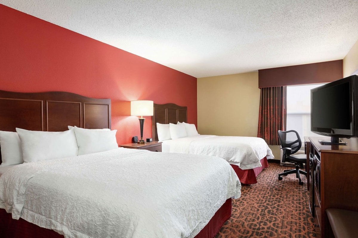 Quarto de hotel com duas camas, uma televisão, uma escrivaninha e uma cadeira.